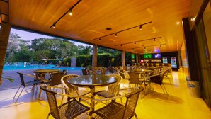 A covered outdoor seating area with tables and chairs, a pool, and a bar area with TVs and a refrigerator. - Falls Galli Hotel (Foz do Iguaçu)