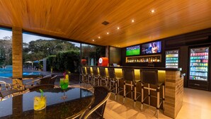 An outdoor bar area with a pool view, bar stools, and a TV screen. - Falls Galli Hotel (Foz do Iguaçu)