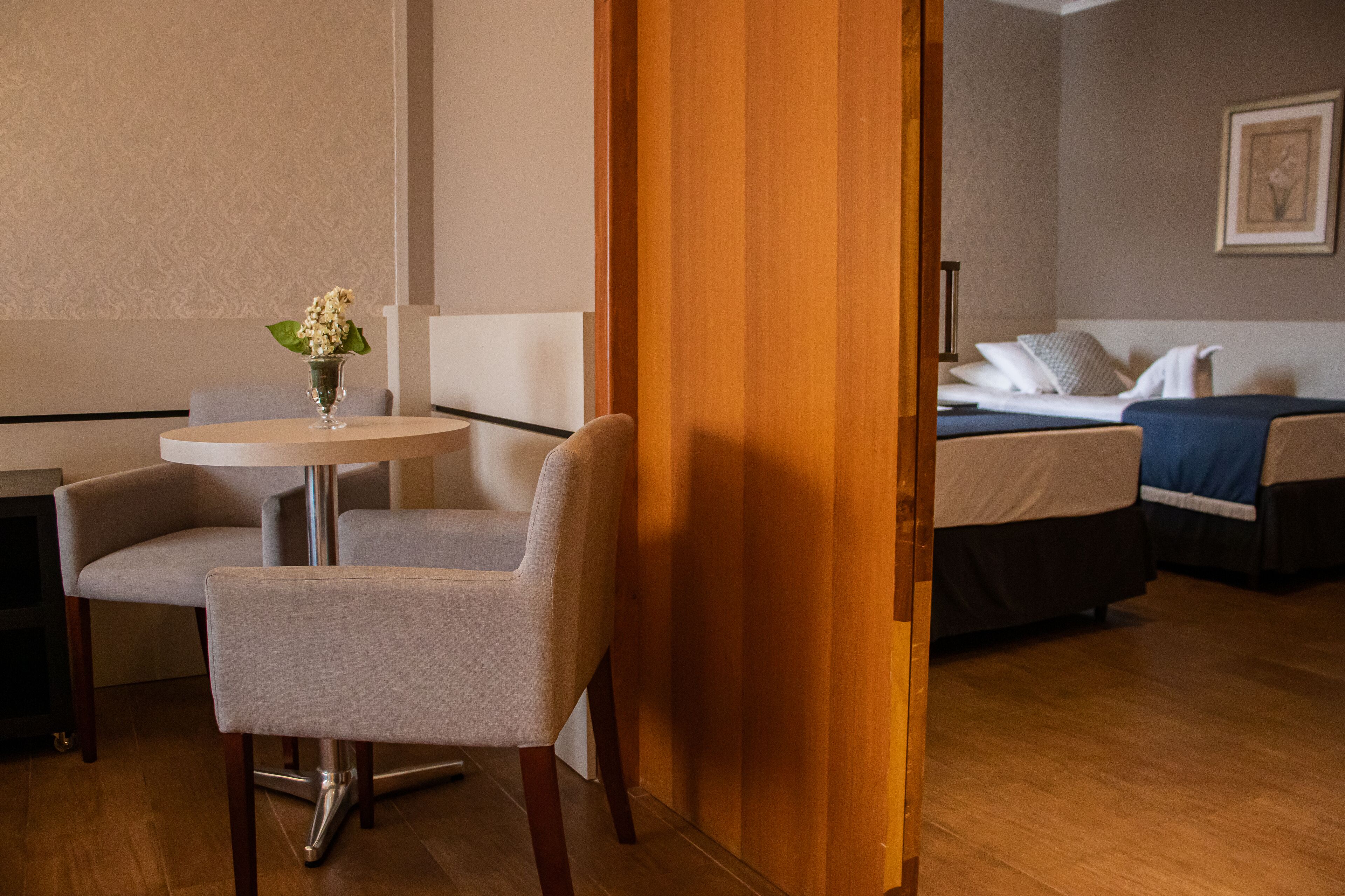 A hotel room with a bed, a bedside table with a vase of flowers, a chair, and a wooden door.