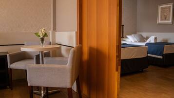 A hotel room with a bed, a bedside table with a vase of flowers, a chair, and a wooden door.