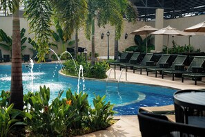 An indoor pool area with lounge chairs and umbrellas, surrounded by plants and a tiled pool. - Nadai Confort Hotel e Spa (Foz do Iguaçu)