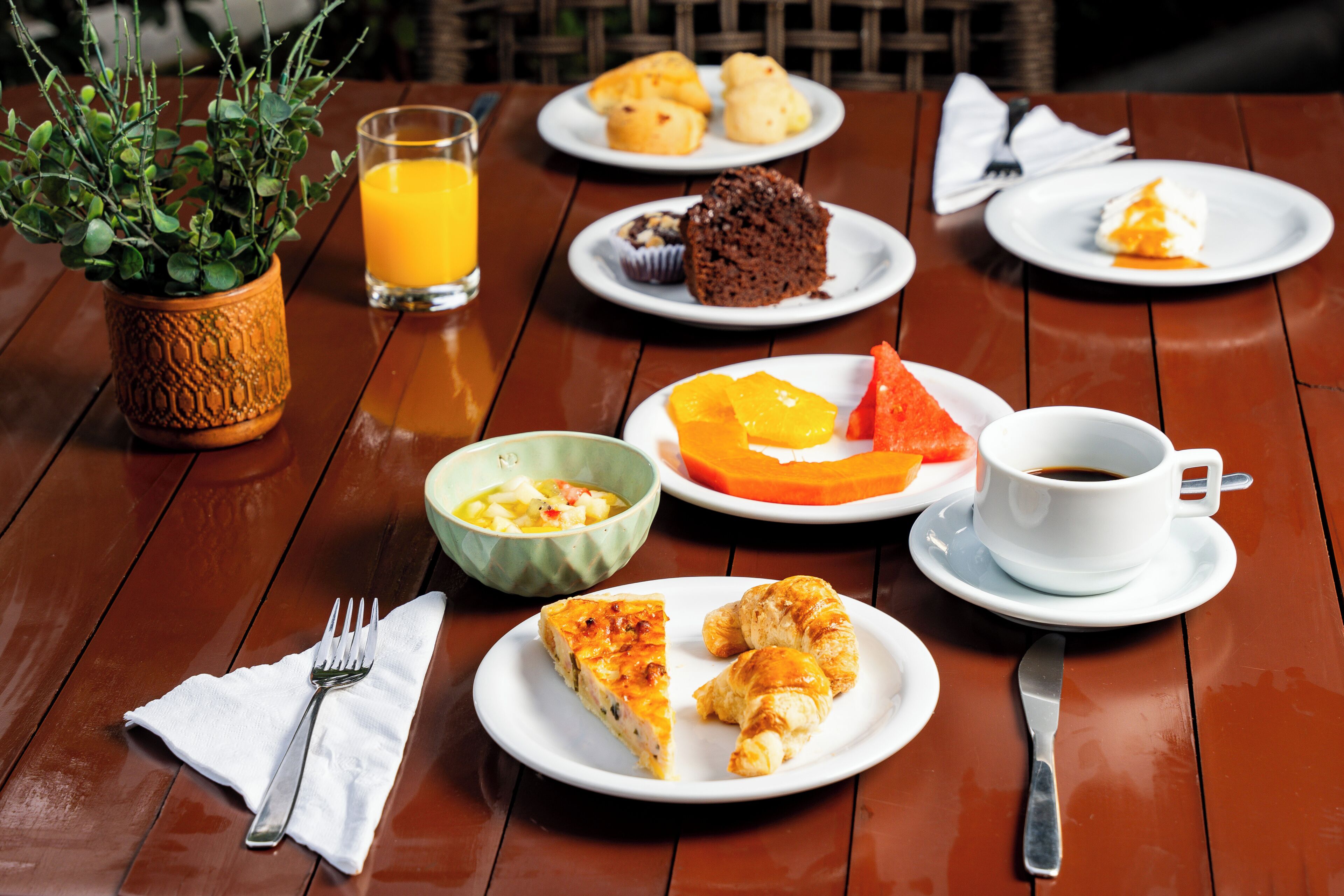 Una mesa de comedor con platos de comida, un vaso de jugo de naranja, una taza de café y una planta.