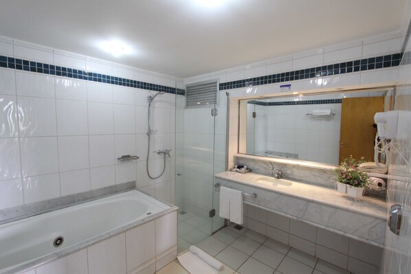 Un baño moderno con bañera, ducha envuelta en cristal, lavamanos de mármol y un espejo grande.
