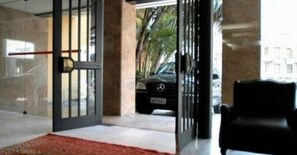 A modern hotel entrance with a glass door, a red carpet, and a parked car outside. - Duque Center Hotel (Porto Alegre)