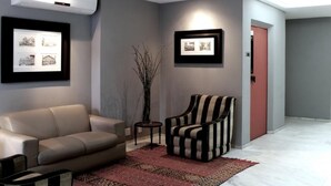 A modern living room with a beige sofa, a striped armchair, and a patterned rug. - Duque Center Hotel (Porto Alegre)
