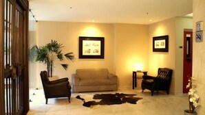 A lobby with a sofa, chairs, a potted plant, framed pictures on the wall, and a cowhide rug. - Duque Center Hotel (Porto Alegre)