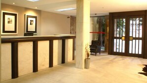 A reception area with a marble counter, framed pictures on the wall, and a large pillar. - Duque Center Hotel (Porto Alegre)