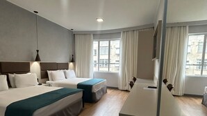 Una habitación de hotel con una cama grande, dos camas más pequeñas, un escritorio y un televisor.