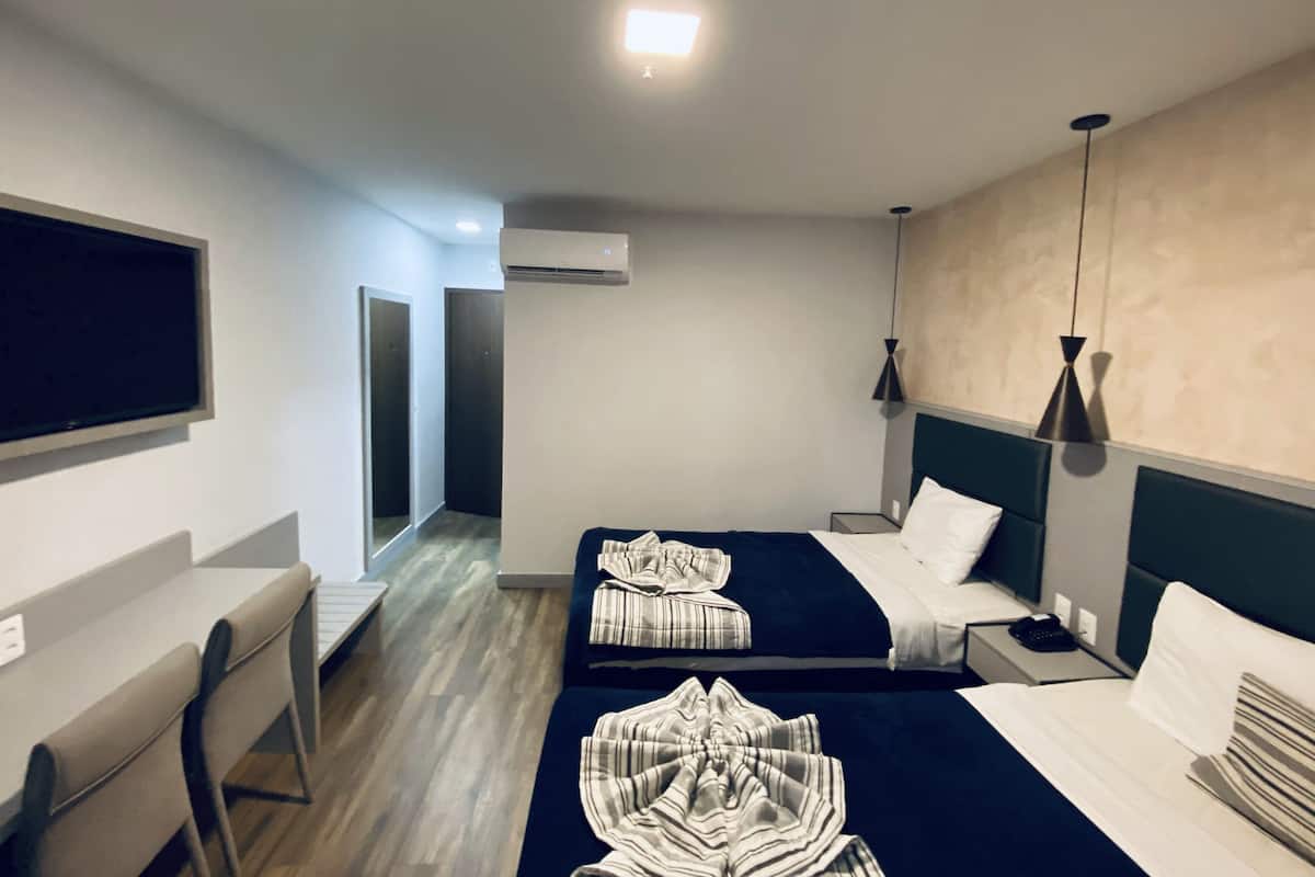 A hotel room with two beds, a desk, a chair, a TV, and an air conditioning unit.