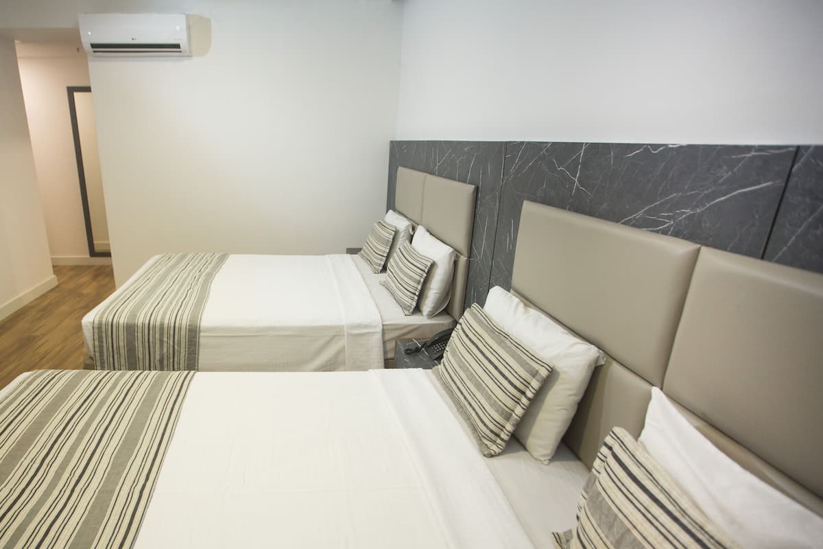 A hotel room with two beds, each with striped bedding and a headboard.