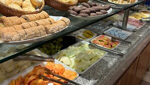 Un bufé con una variedad de alimentos, como pan, pasteles, frutas y verduras.