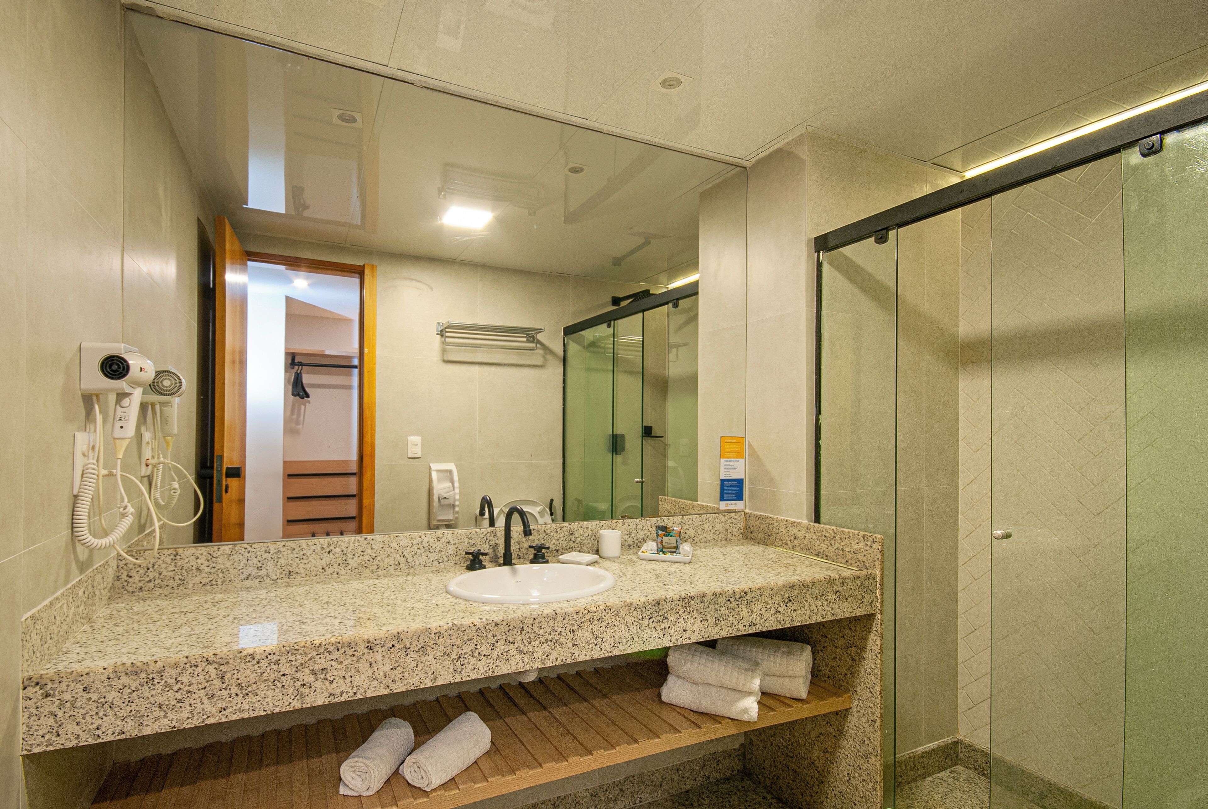 A bathroom with a granite countertop, two sinks, a glass shower enclosure, and a towel rack.