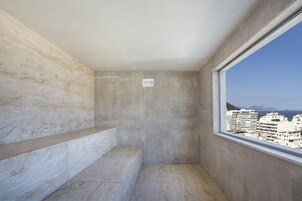 A small, modern room with a concrete wall, a window, and a view of buildings.
