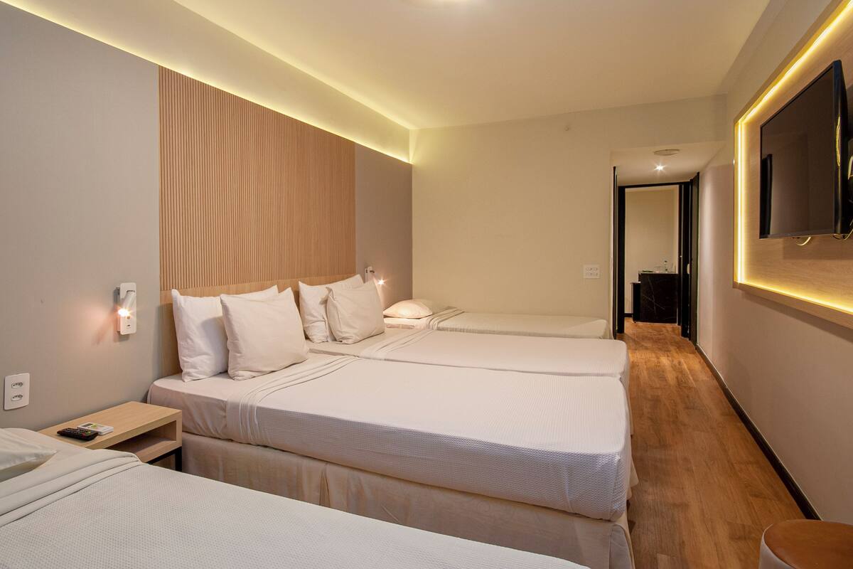 Une chambre d’hôtel avec deux lits, une tête de lit en bois, un téléviseur à écran plat et une table de chevet avec une lampe.