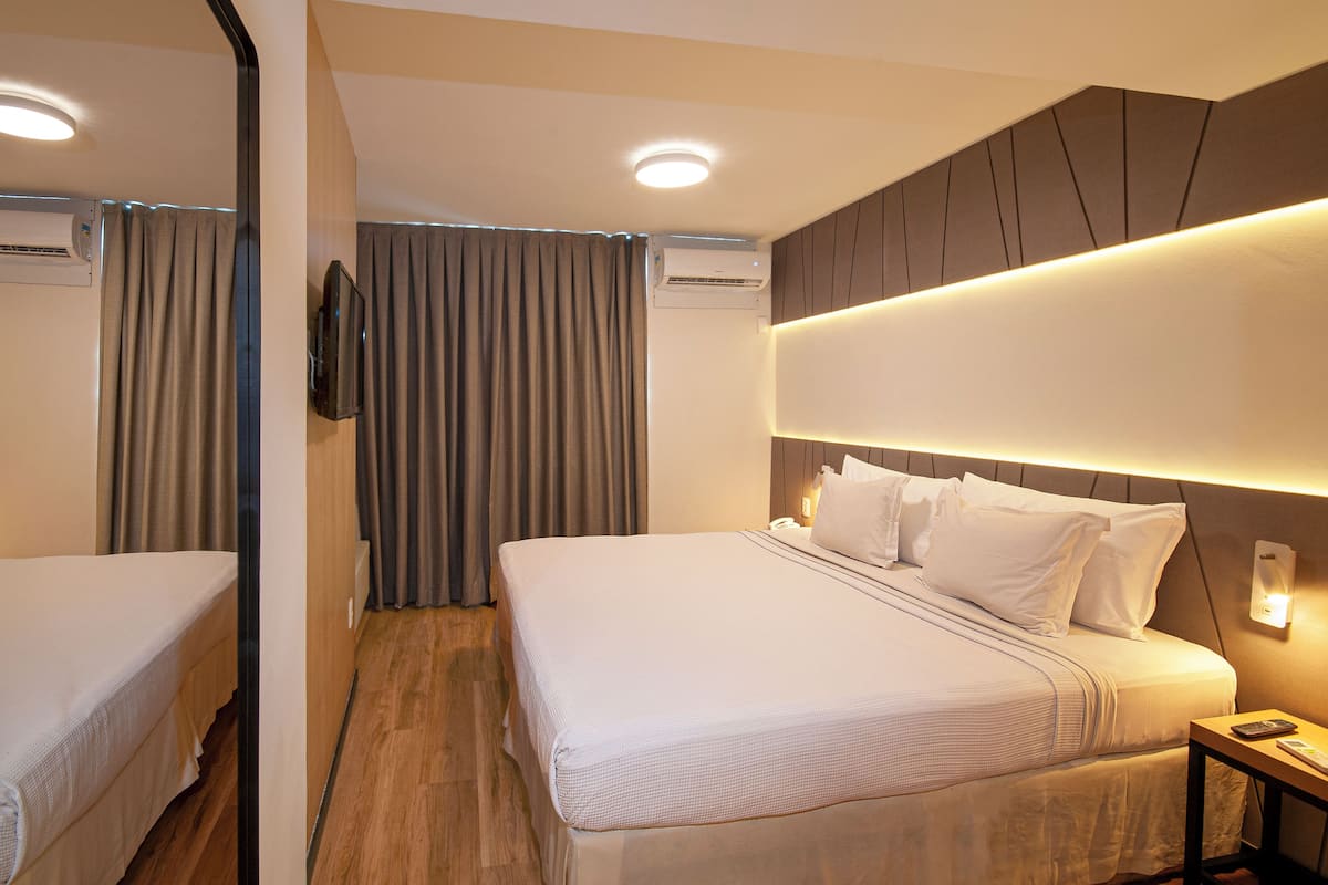 Een hotelkamer met een groot bed, een nachtkastje, een aan de muur bevestigde televisie en een airconditioning.