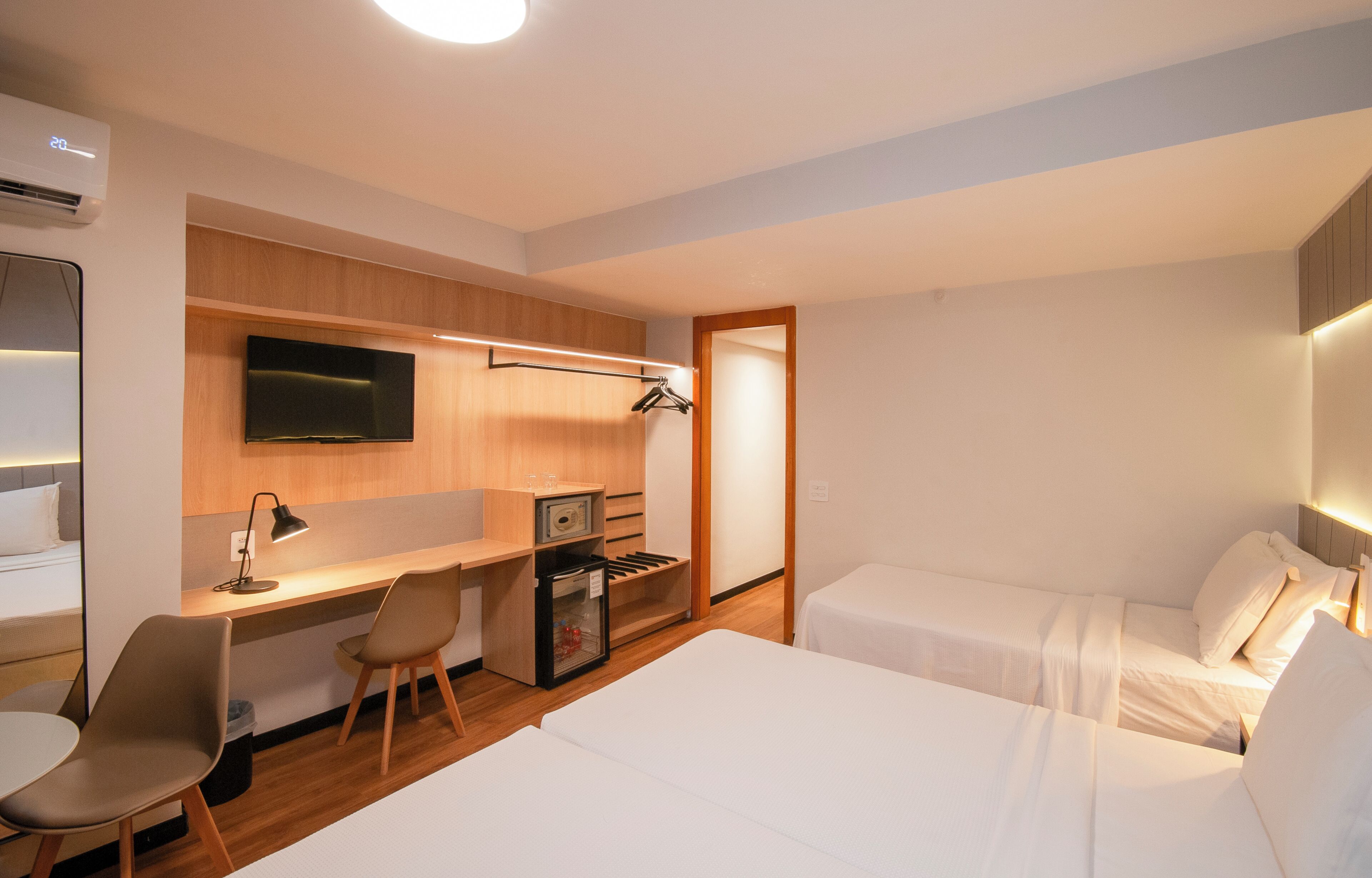 A hotel room with a bed, a desk with a chair, a TV, and a minibar.