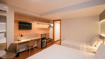 A hotel room with a bed, a desk with a chair, a TV, and a minibar.