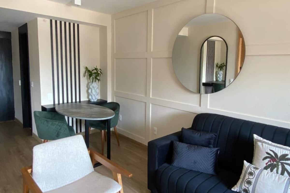 Een moderne woonkamer met een donkerblauwe bank, een ronde spiegel en een eethoek met een kleine tafel en stoelen.