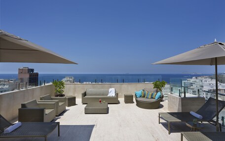 A rooftop terrace with outdoor seating, including sofas and chairs, and a view of the ocean.