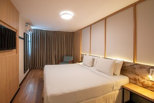 Una habitación de hotel con una cama, una silla, un televisor y aire acondicionado instalado en la pared.