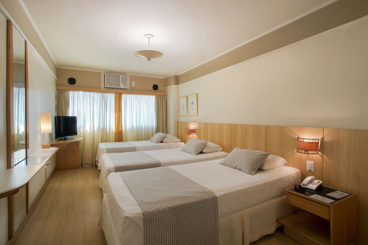 Een hotelkamer met twee bedden, een televisie, bureau, telefoon en een wandlamp.