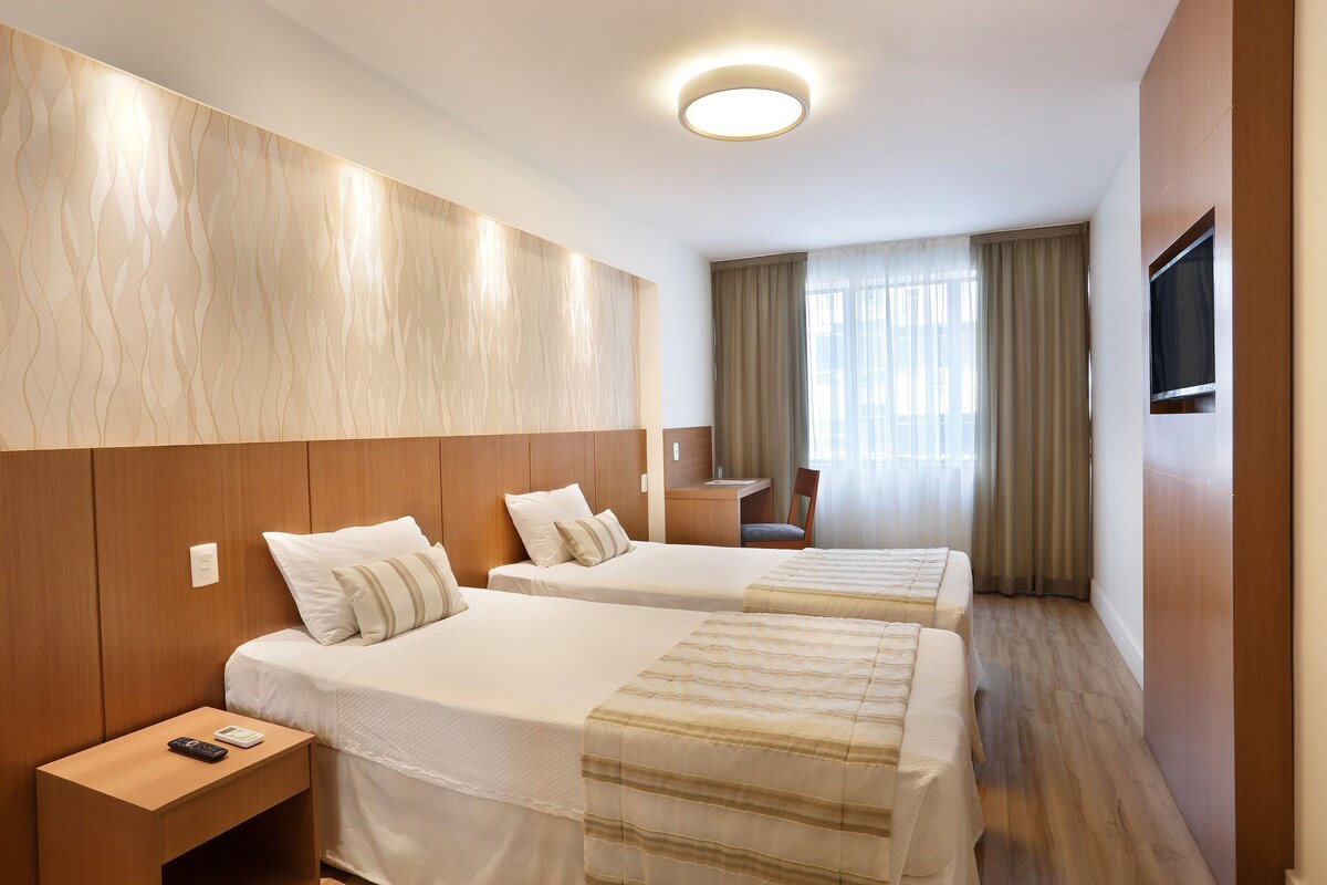 Une chambre d’hôtel avec deux lits, un bureau, une chaise et un téléviseur.