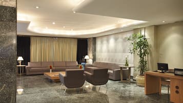 Een moderne hotel lobby met een zithoek, een salontafel, een bureau en een grote kamerplant.