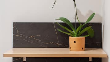 A corner with a wooden shelf holding a potted plant and a grey ottoman with wooden legs.