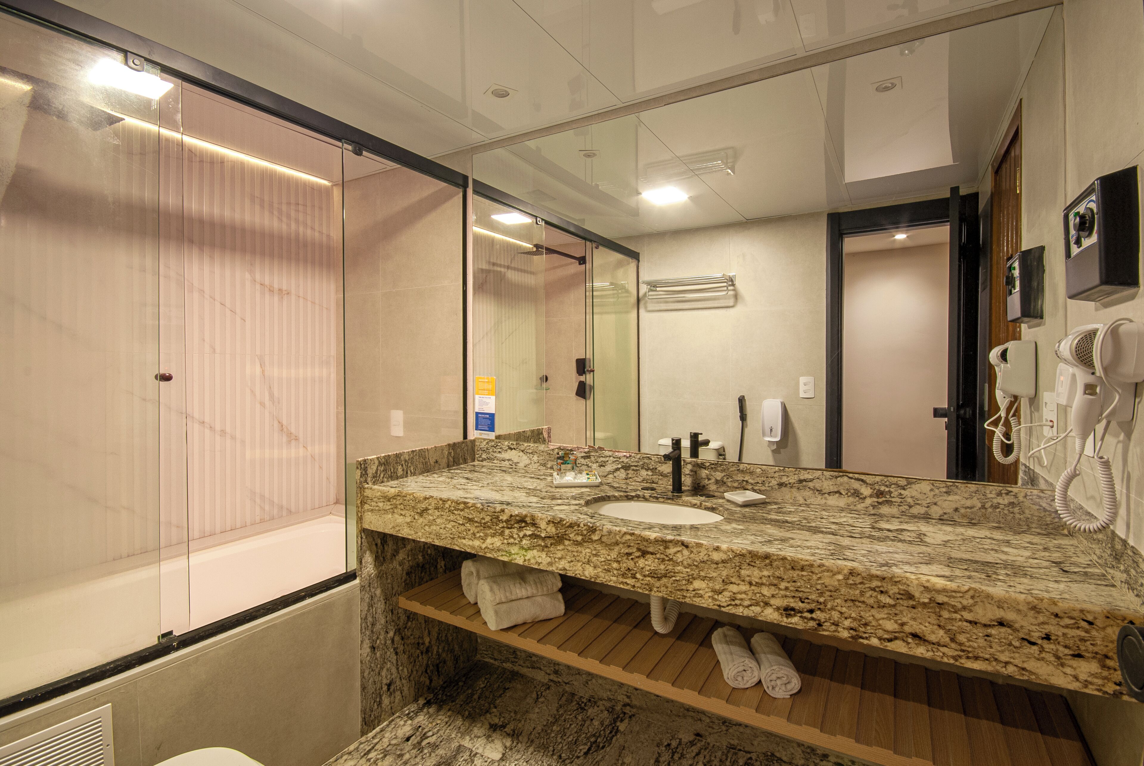A bathroom with a marble countertop, a sink, a mirror, a towel rack, and a shower area.