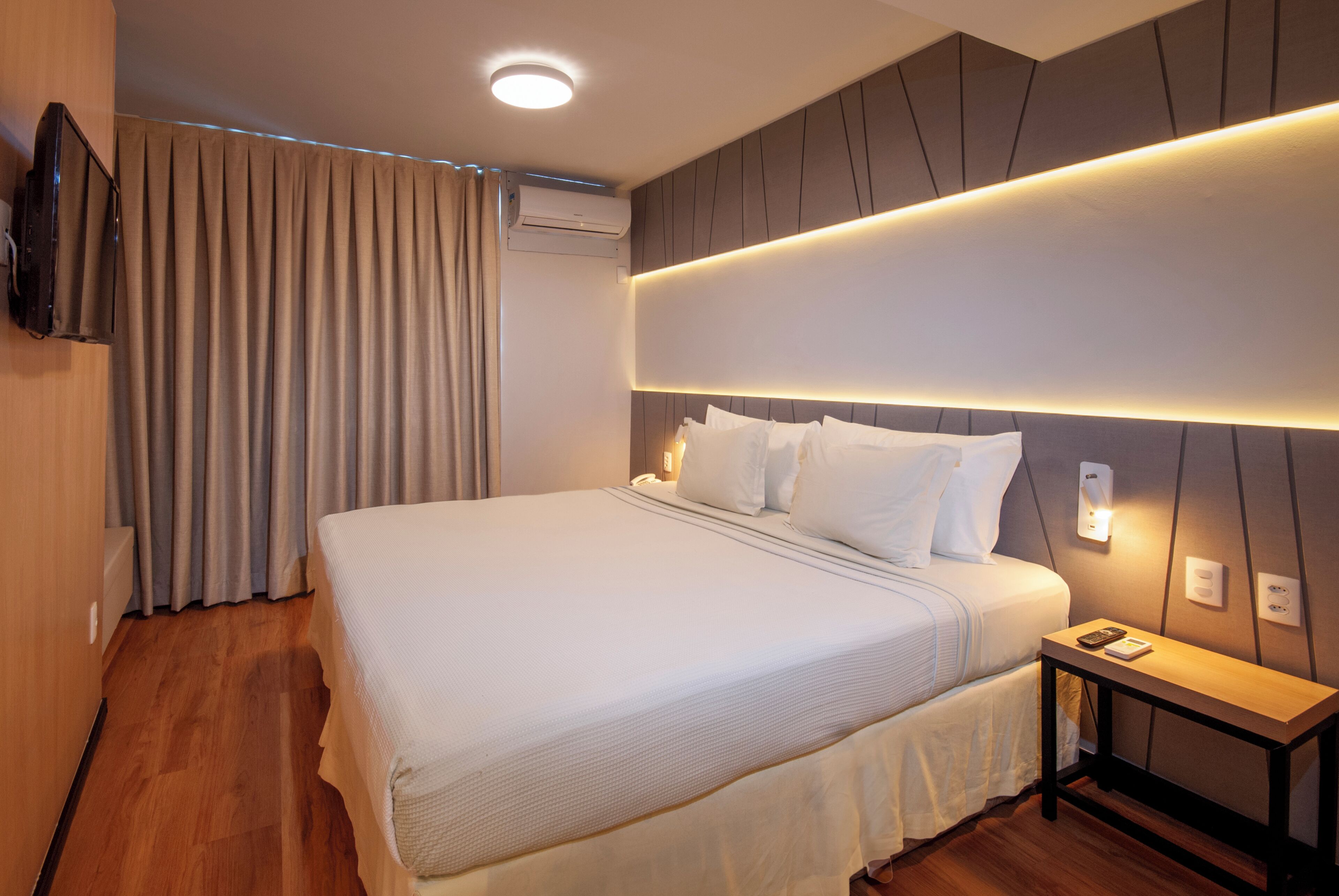 Une chambre d’hôtel dotée d’un grand lit, d’une table de chevet, d’un téléviseur à écran plat fixé au mur et d’un appareil de climatisation.