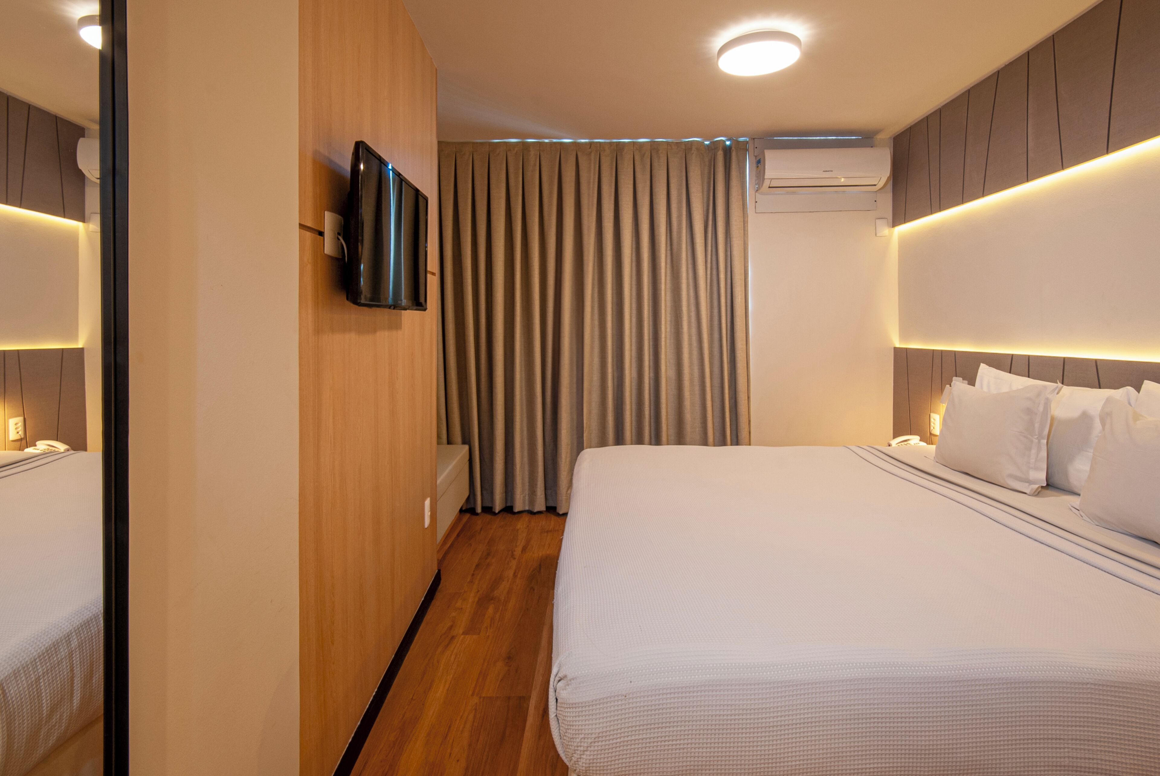 Een hotelkamer met een bed, een televisie, een airconditioner en een gordijn.