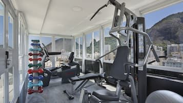 A gym with exercise equipment and large windows overlooking a cityscape.