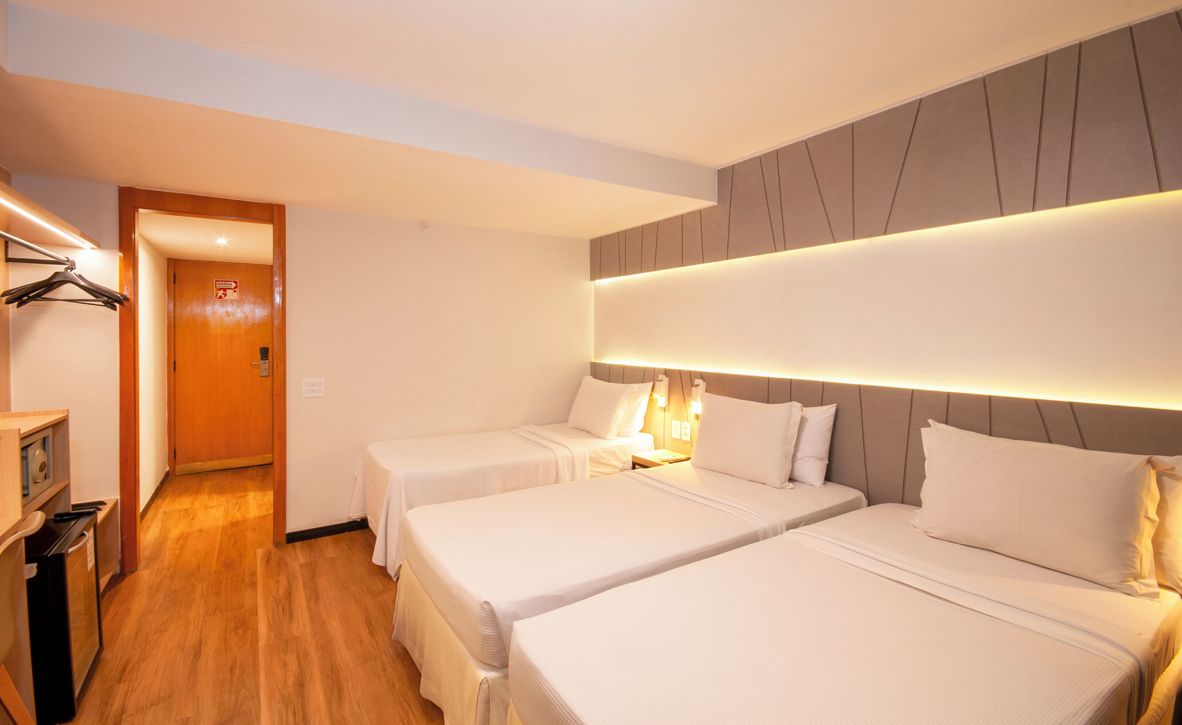 Habitación de hotel con dos camas, piso de madera, un pasillo con una puerta y una pequeña kitchenette.