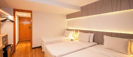Habitación de hotel con dos camas, piso de madera, un pasillo con una puerta y una pequeña kitchenette.