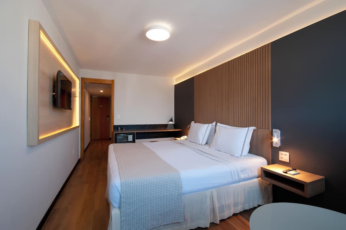 Een moderne hotelkamer met een groot bed, nachtkastje, televisie aan de muur en een klein bureau.