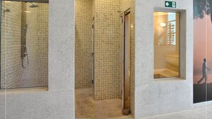 A modern bathroom with a shower, tiled walls, and a glass door leading to a hallway. - Piemonte Hotel (Nova Lima)