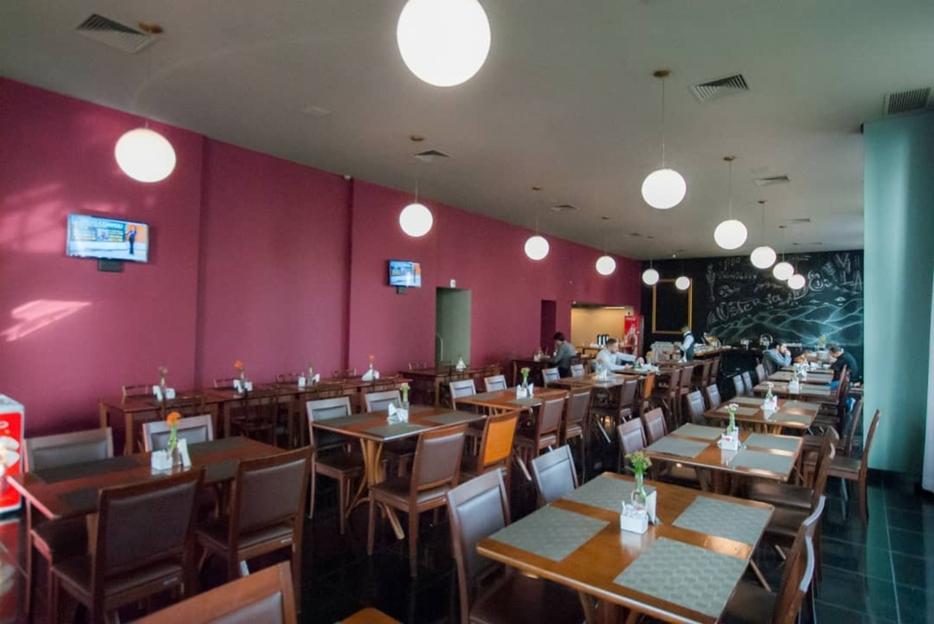 A restaurant with multiple tables and chairs, a chalkboard wall, and ceiling lights.