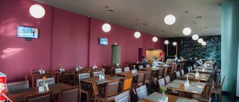 A restaurant with multiple tables and chairs, a chalkboard wall, and ceiling lights.