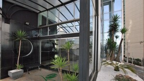 A modern building with large glass windows, indoor plants, and a paved entrance area. - Piemonte Hotel (Nova Lima)