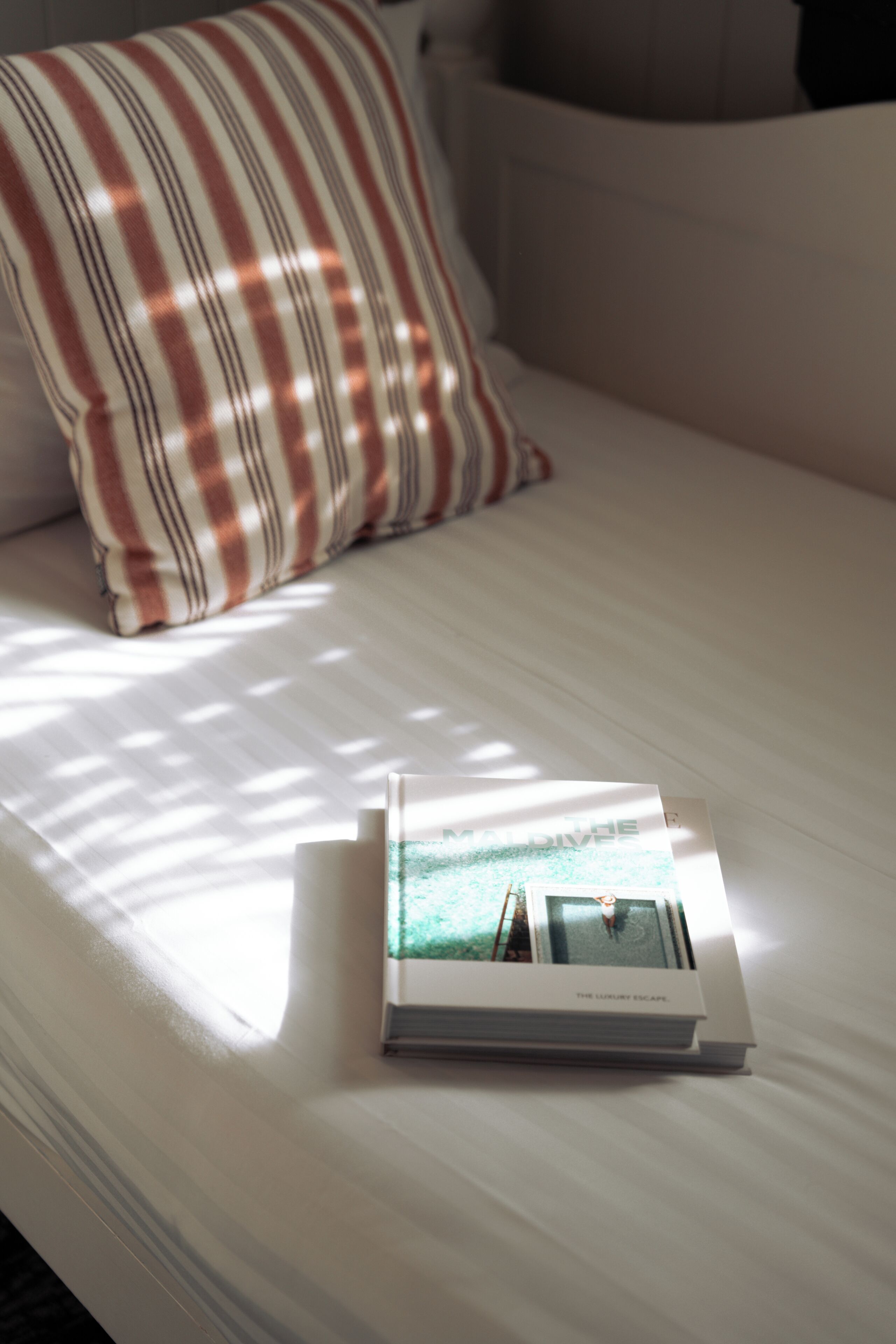 Cama bem arrumada com almofada listrada e um livro intitulado 'The Luxury Escape' em cima.
