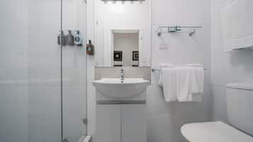 A modern bathroom with a white sink, mirror, and toilet. There are toiletries on the wall and a glass shower enclosure.