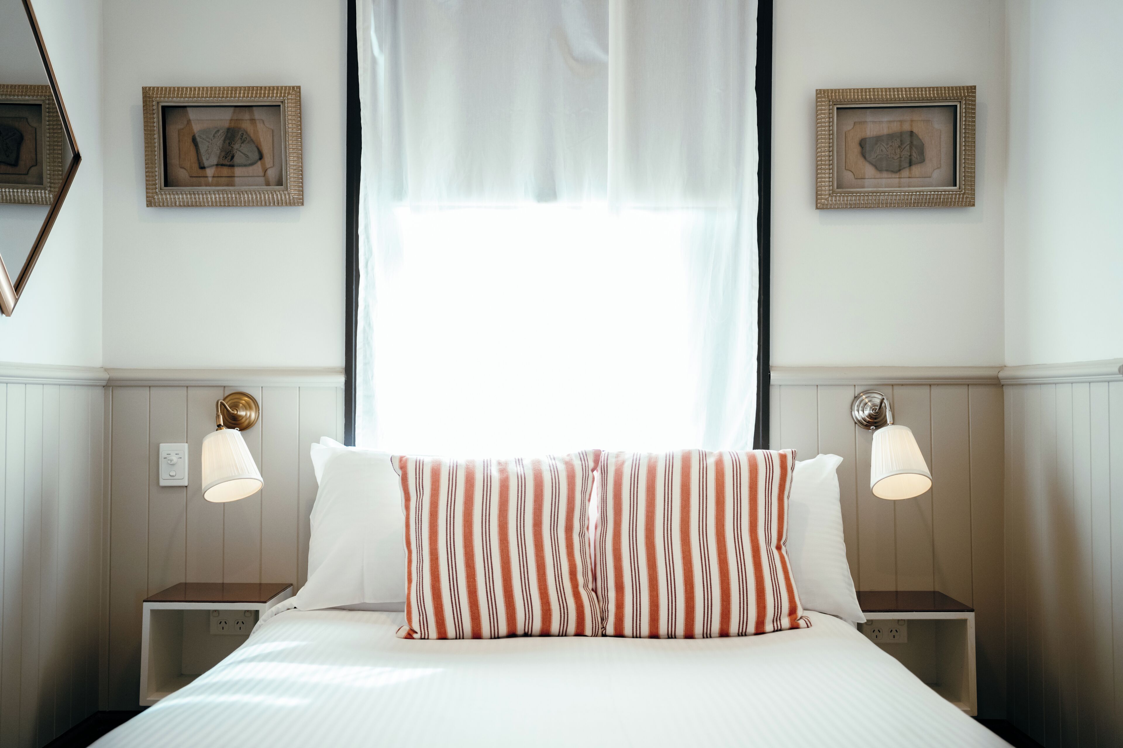 Une chambre d’hôtel avec un lit, deux tables de chevet, une fenêtre avec des rideaux légers et des lampes fixées au mur.