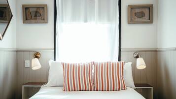 Une chambre d’hôtel avec un lit, deux tables de chevet, une fenêtre avec des rideaux légers et des lampes fixées au mur.