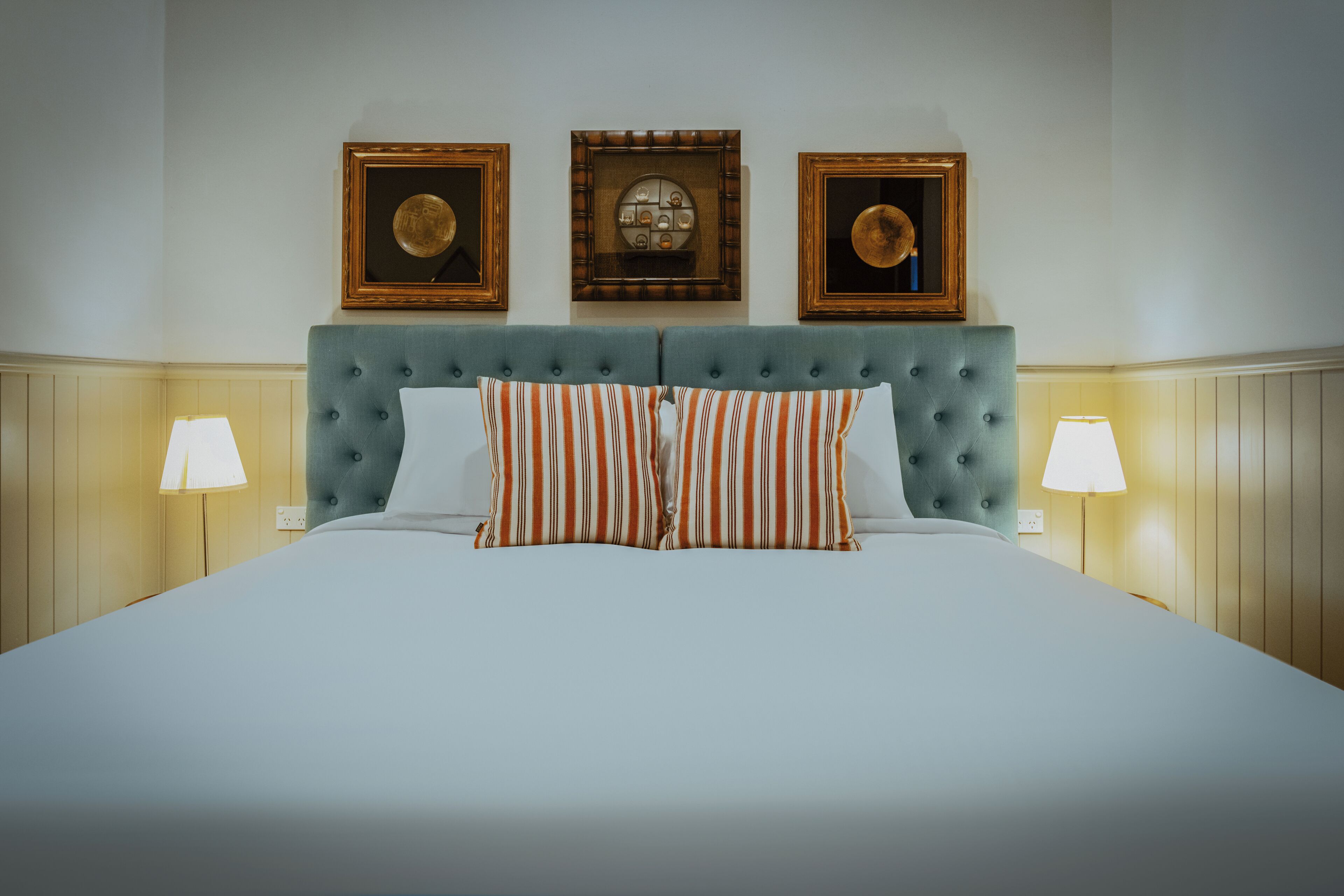 Una cama impecablemente arreglada con almohadillas a rayas, un cabecero capitonado y dos lámparas de pared a cada lado.