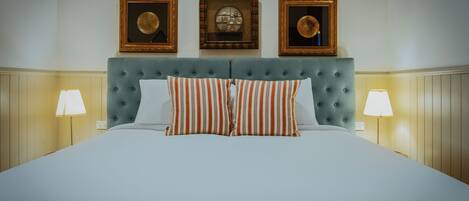 Cama bem arrumada com almofadas listradas, cabeceira estofada e duas luminárias fixadas nas paredes de cada lado.