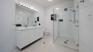 A modern bathroom with a glass-enclosed shower, white cabinetry, and a large mirror with lights above.
