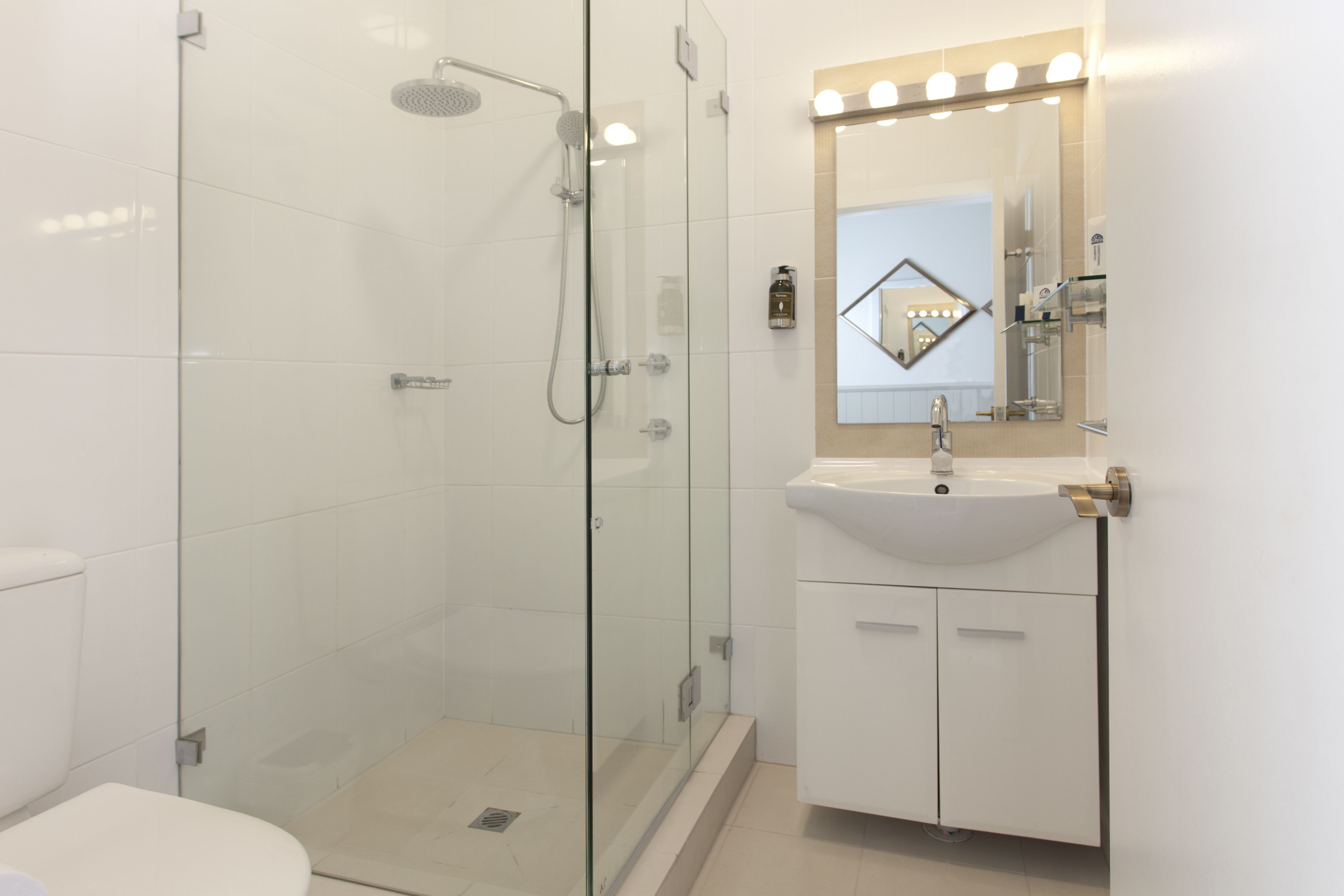 Un baño moderno con ducha envuelta en vidrio, un lavabo blanco con espejo encima y un inodoro.