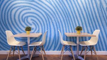 A dining area with a spiral blue wallpaper, two white chairs, and a small yellow table with a potted plant.