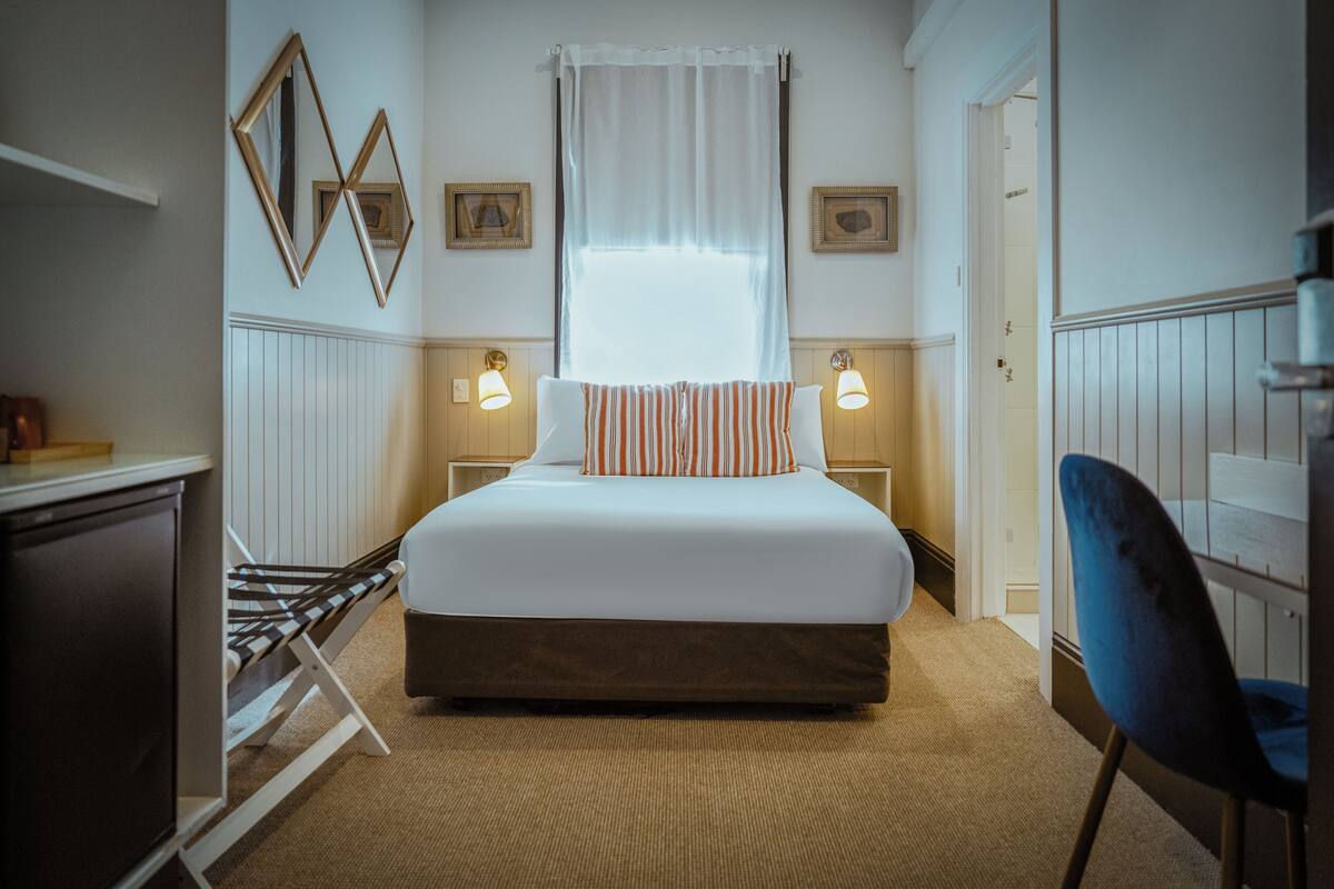 Ein ordentlich eingerichtetes Schlafzimmer mit Bett, Nachttischlampen, einem Sessel und einem Kleiderschrank.