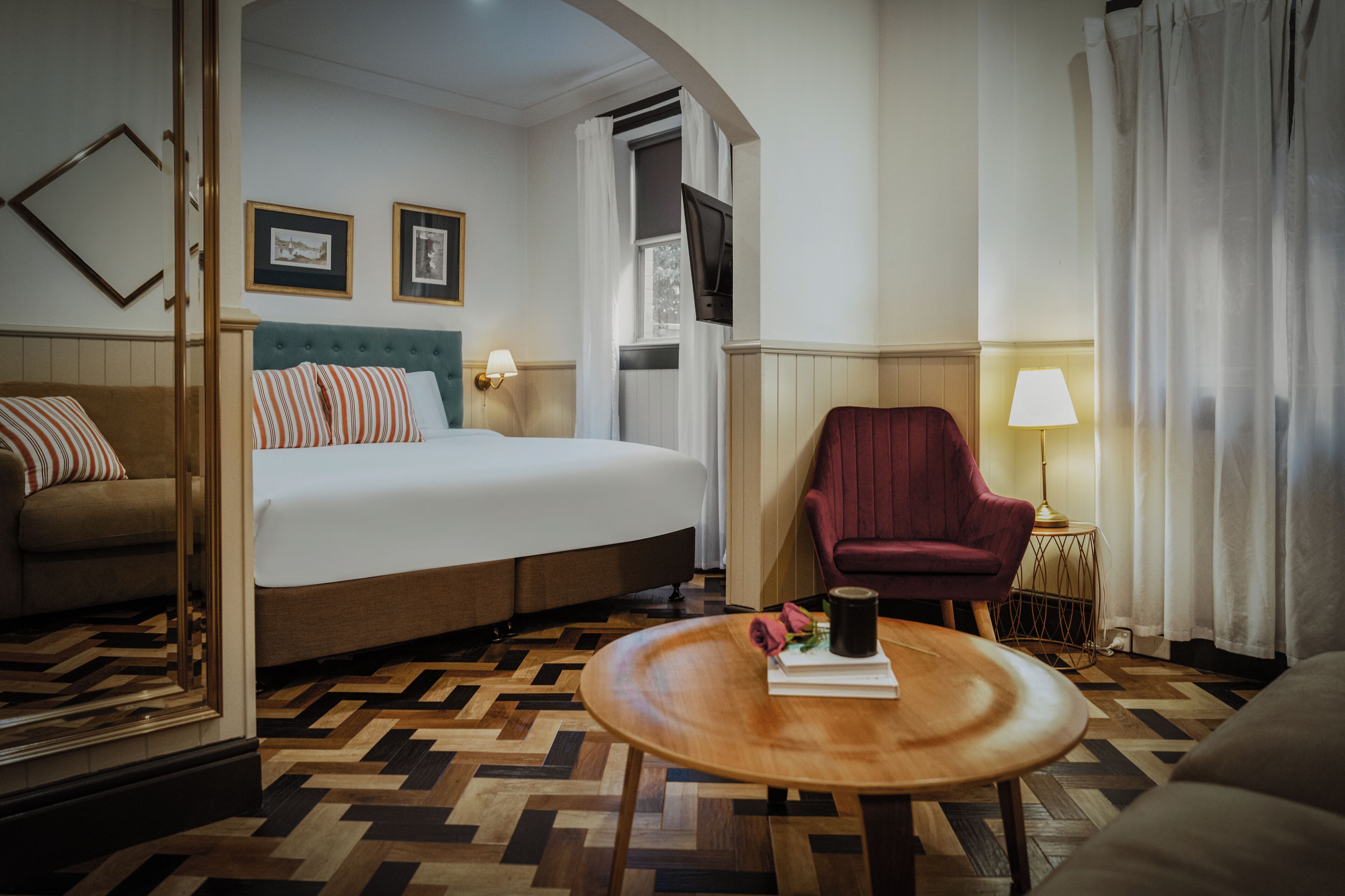 A hotel room with a bed, a sofa, a chair, a round table, and a TV.